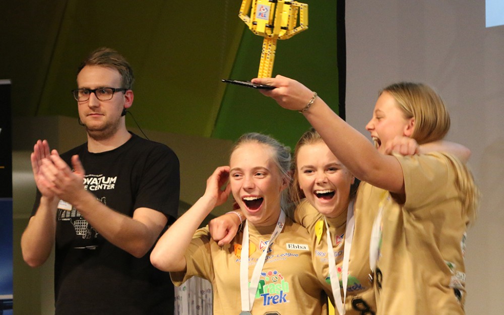 Tre tjejer med medaljer om halsen håller upp en pokal